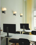In a mint-green office, three black Clérachic wall lights glow above standing desks with monitors.