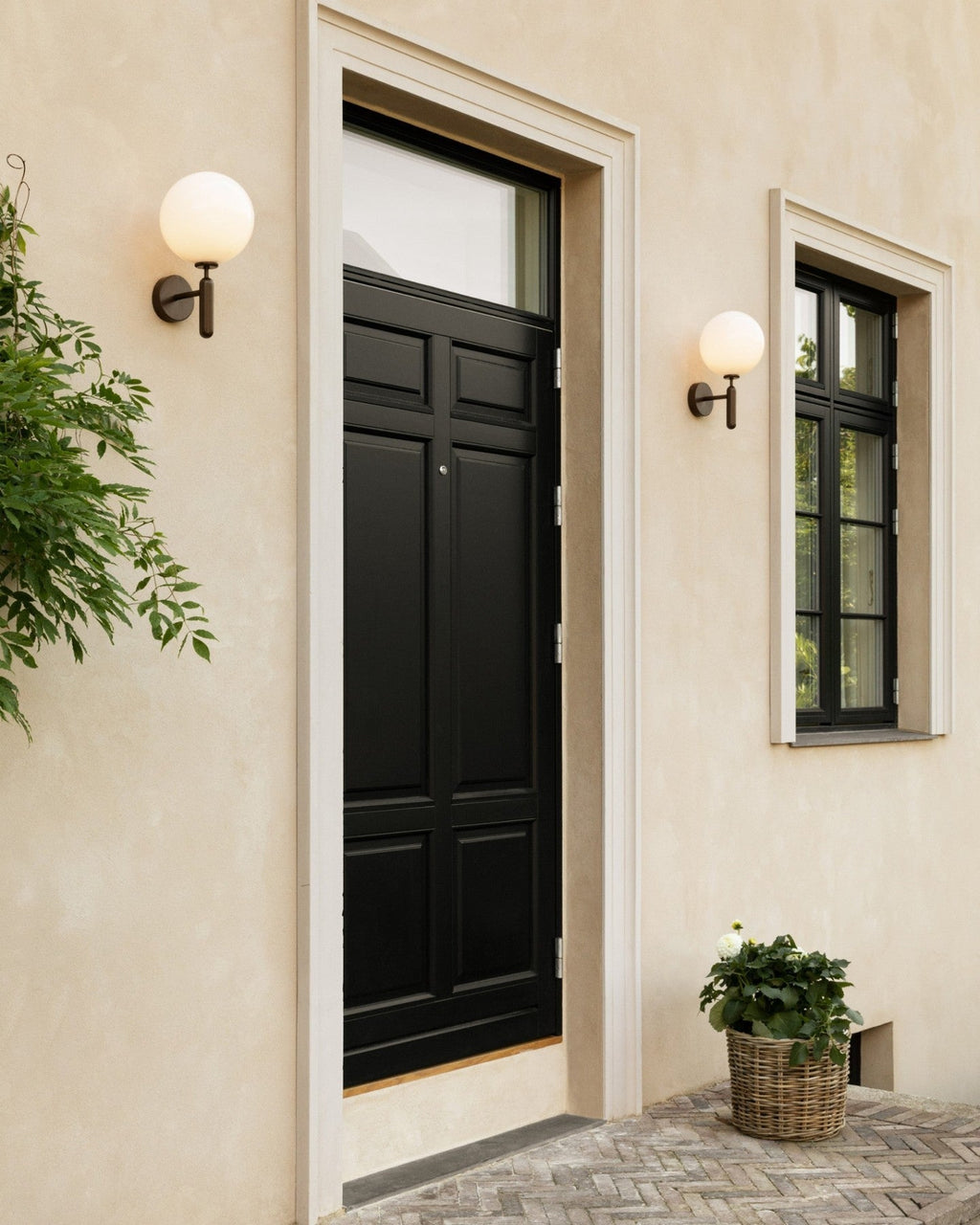 Either side of a black front door, two black Clérachic wall lights glow against a beige stucco facade.