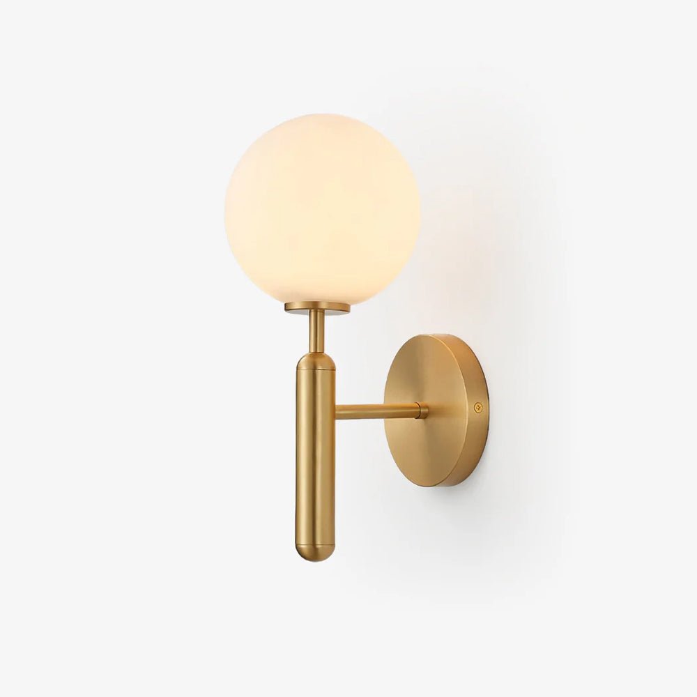 A brushed brass Clérachic wall light with a round white glass globe, shown straight-on against a plain cream wall.