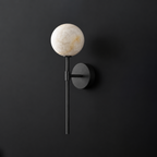Cutout view of this Clérachic wall sconce in black, its alabaster ball shade glowing against a dark wall.
