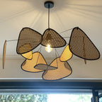 Greenery is visible through a tall window behind this Clérachic pendant, its bulb glowing beneath dark and tan paddles.