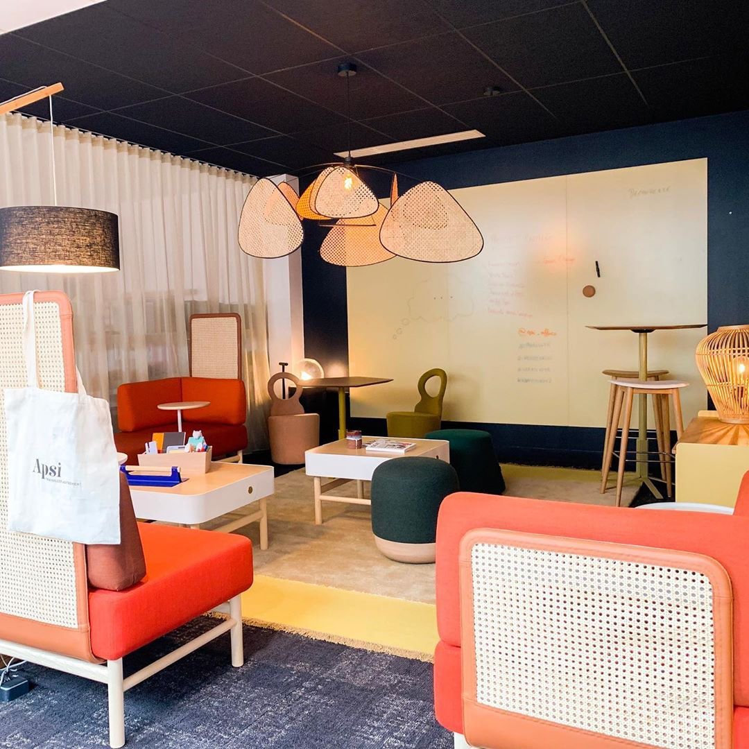 In a lounge furnished with an orange armchair and cane table, this Clérachic pendant hangs above sheer curtains.