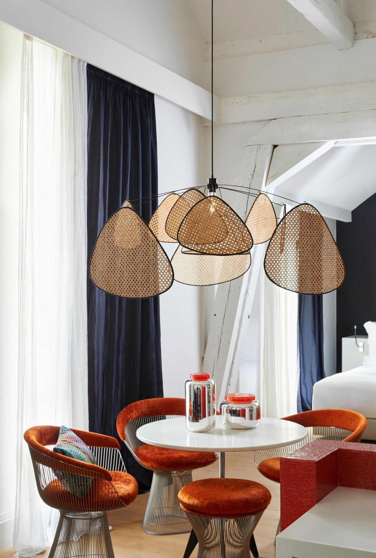 Under a sloped white ceiling, this Clérachic pendant hangs low over a round table ringed with rust-orange stools.