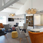 A high beamed ceiling holds this Clérachic pendant above a lounge furnished with mustard and grey armchairs.