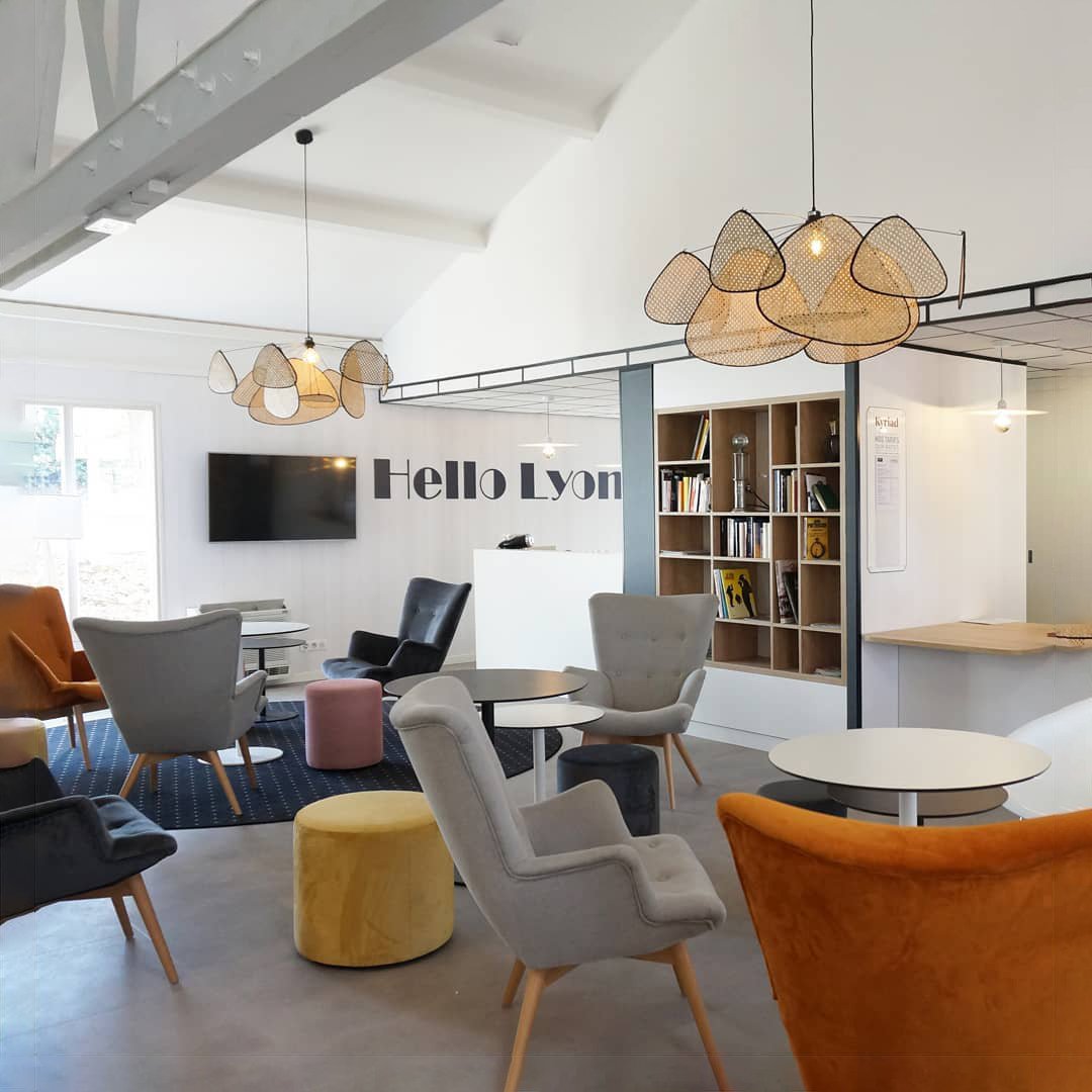 A high beamed ceiling holds this Clérachic pendant above a lounge furnished with mustard and grey armchairs.