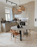 This Clérachic pendant hangs above a round marble table with mismatched dining chairs in a light-toned kitchen.