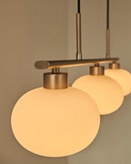 Three white glass globes lit along a horizontal pendant bar