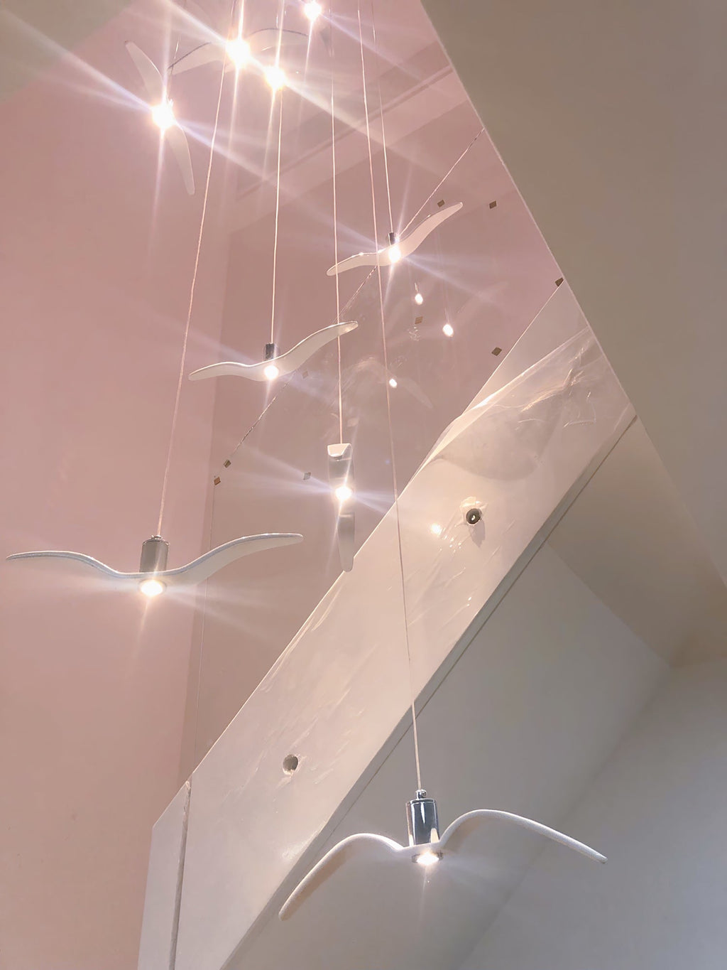 Bird-shaped pendants from this Clérachic light hang down a stairwell, with pinpoints of light sparkling above.
