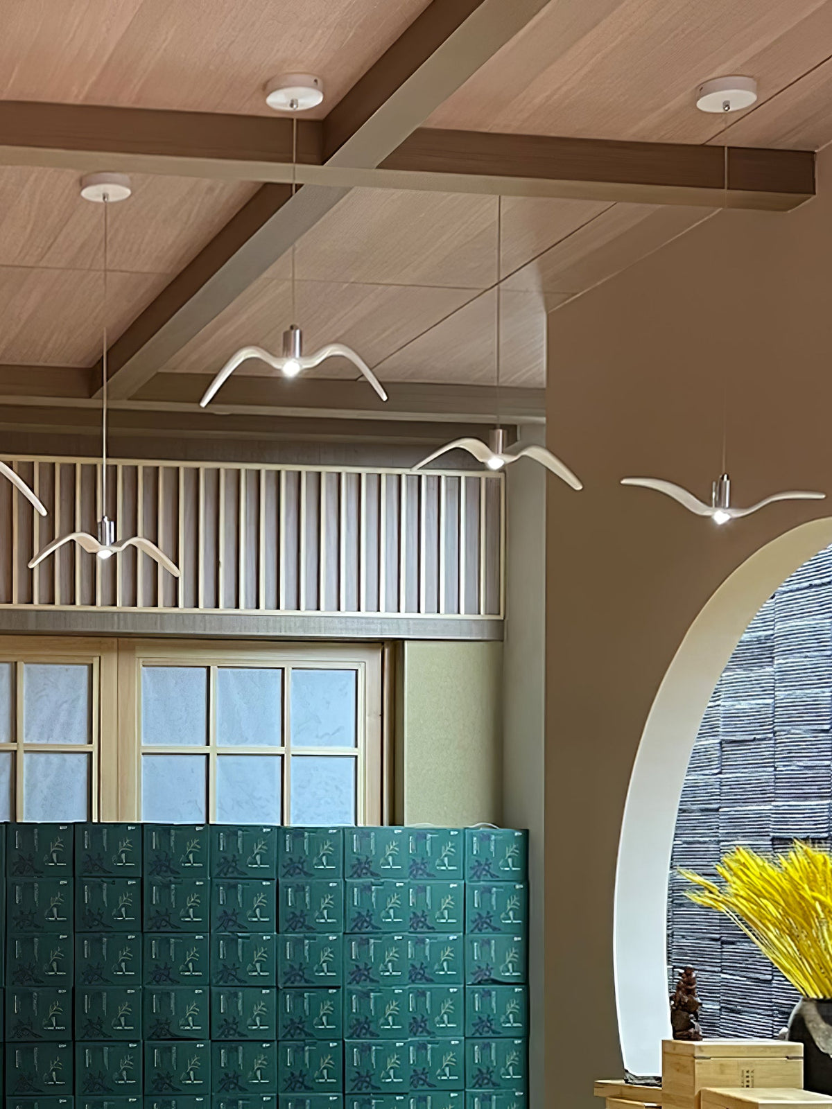 A white bird-shaped pendant from this Clérachic light hangs on a balcony landing near a teal tiled wall and arched doorway.