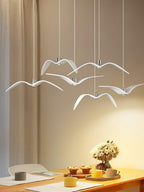 White bird-shaped pendants from this Clérachic fixture hang above a breakfast table set with cups and fresh flowers.