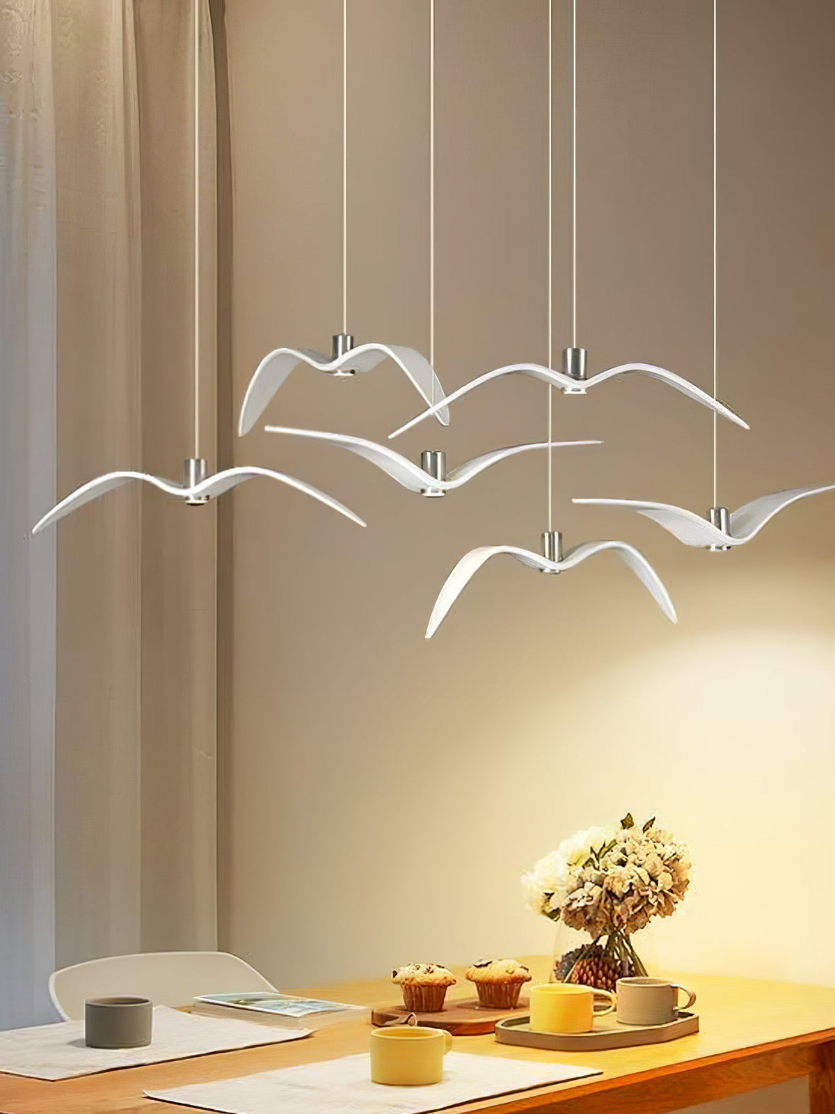 White bird-shaped pendants from this Clérachic fixture hang above a breakfast table set with cups and fresh flowers.