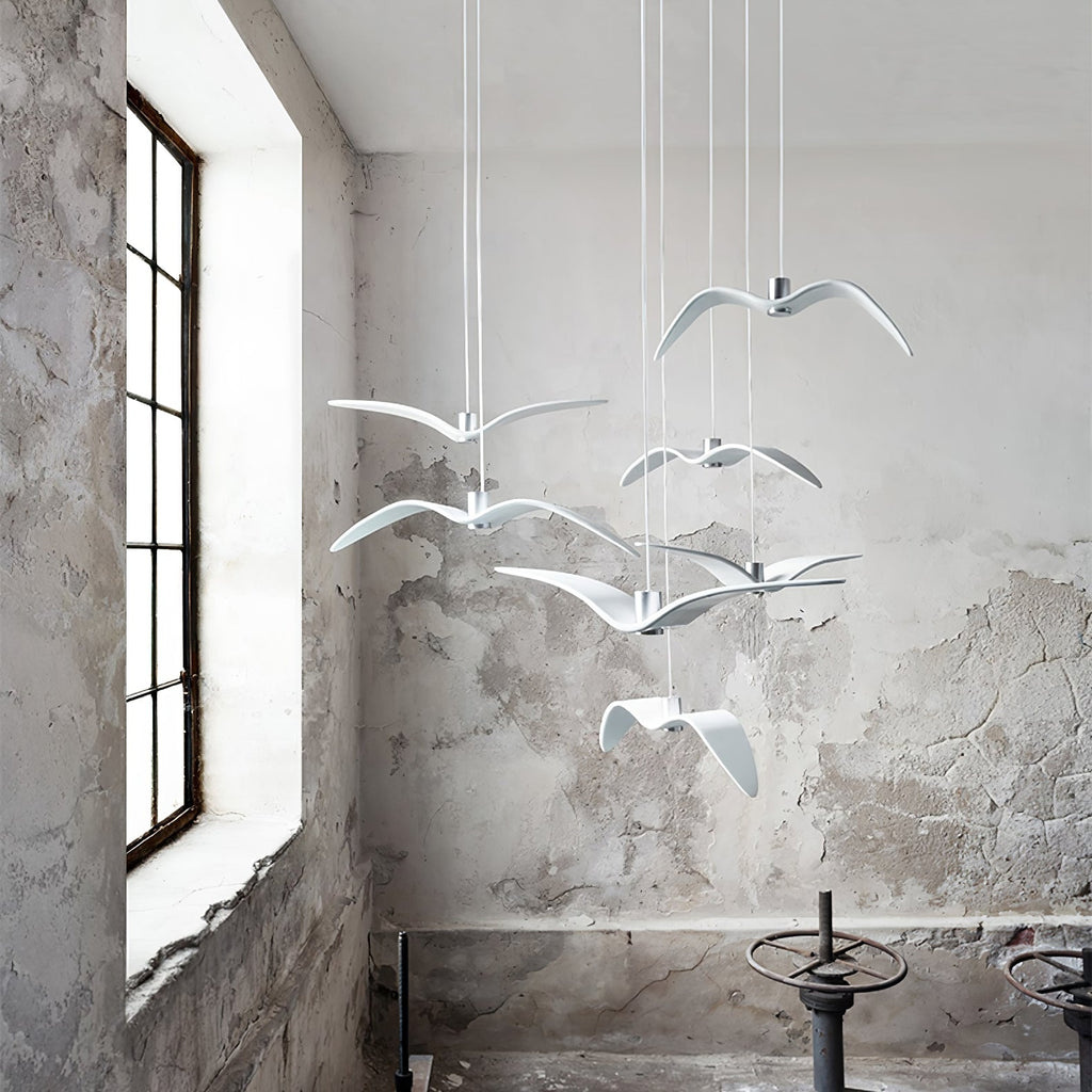 White bird pendants from this Clérachic fixture hang in a loft-style room with a large window and weathered plaster wall.