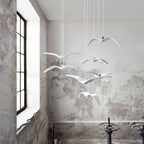 White bird pendants from this Clérachic fixture hang in a loft-style room with a large window and weathered plaster wall.