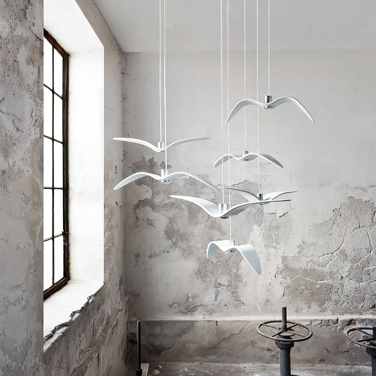 White bird pendants from this Clérachic fixture hang in a loft-style room with a large window and weathered plaster wall.