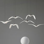 White bird-shaped pendants from this Clérachic fixture hang above a plain white sphere, on a grey backdrop.