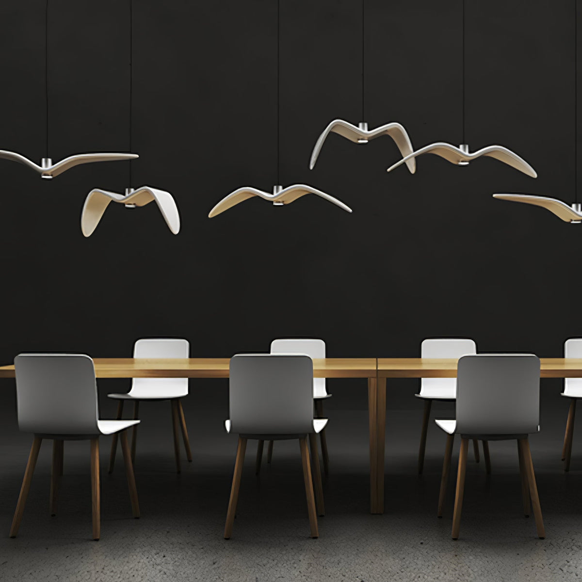 White bird-shaped pendants from this Clérachic fixture hang above a long table with grey chairs, on a dark backdrop.