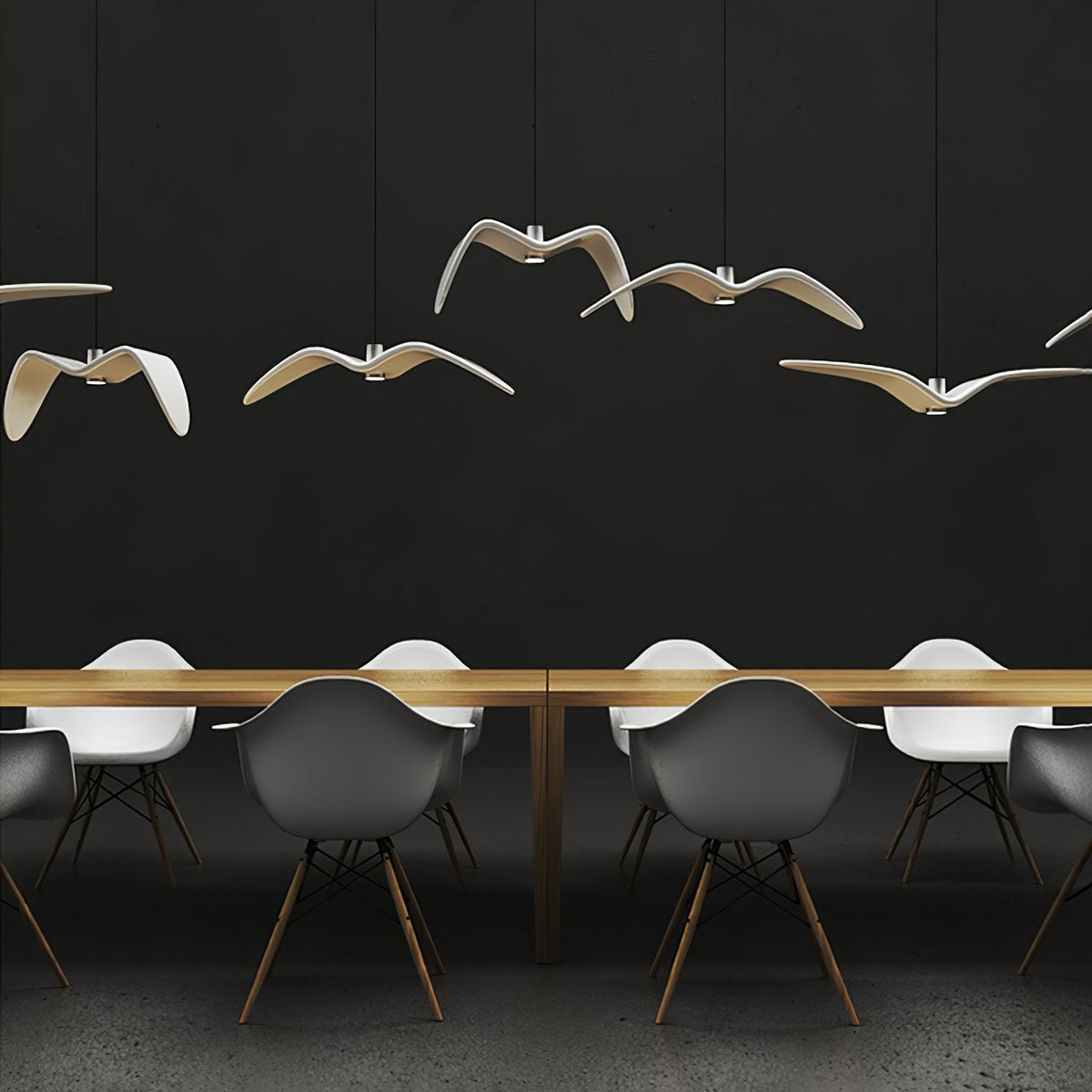 A cluster of white bird pendants from this Clérachic light hangs above a long wooden table with white chairs, on a dark backdrop.