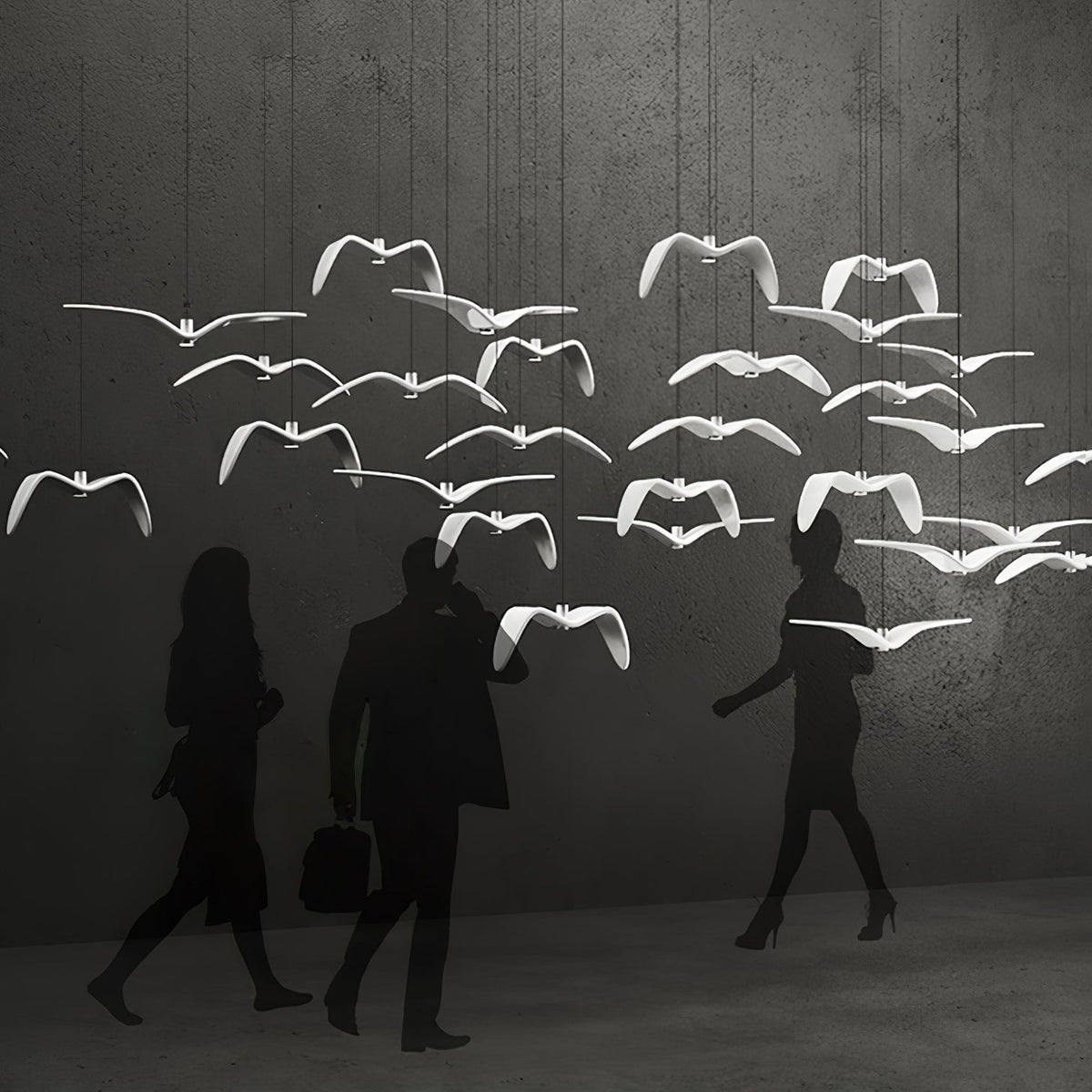 A flock of white bird pendants from this Clérachic light hangs above walking figures silhouetted against a grey backdrop.