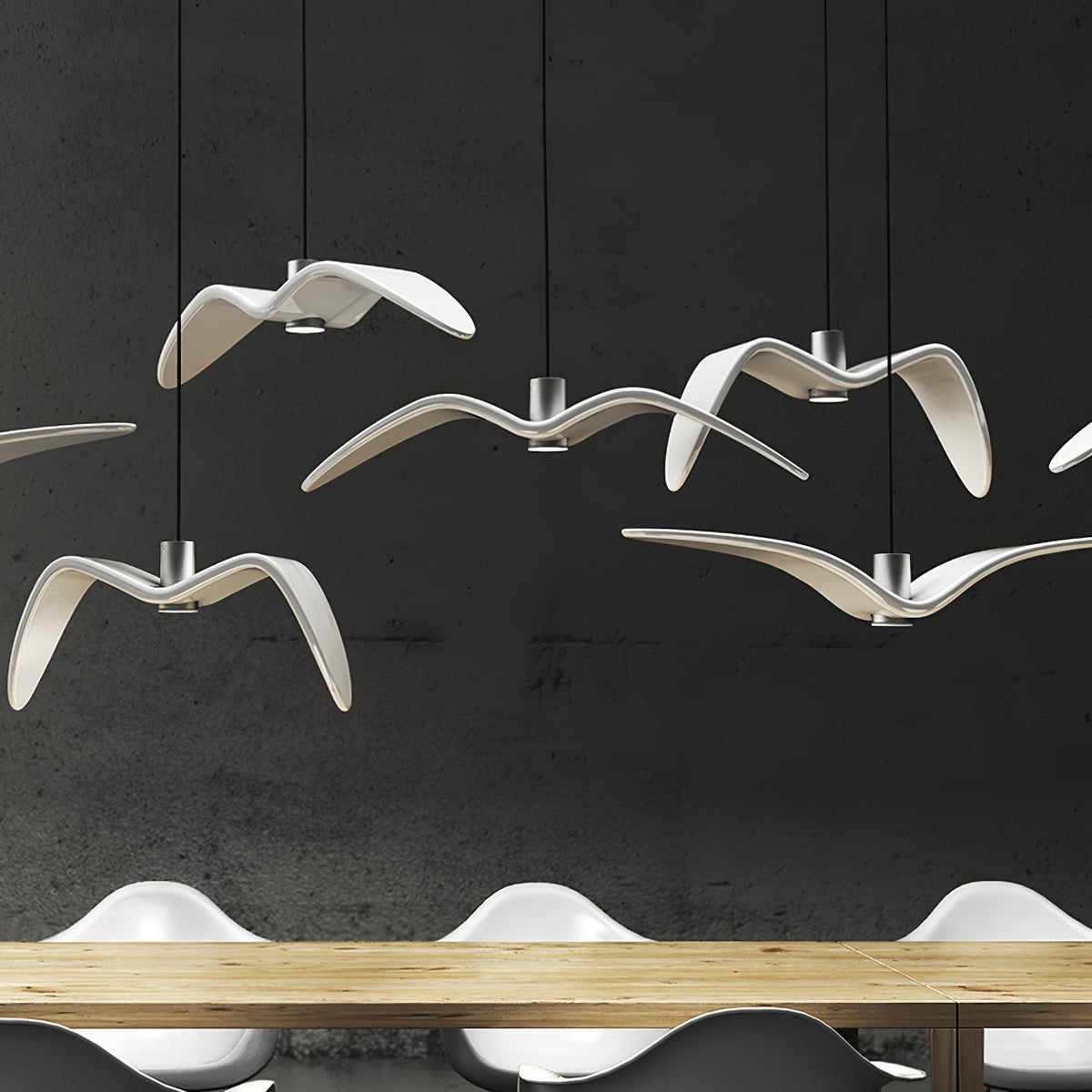 White bird-shaped pendants from this Clérachic fixture hang low above a wooden table, seen close against a dark backdrop.