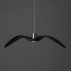 A black bird-shaped pendant from this Clérachic light hangs front-on with wings spread, on a plain dark-grey backdrop.