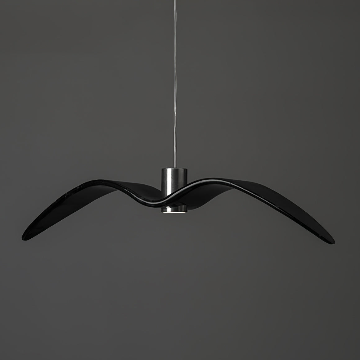 A black bird-shaped pendant from this Clérachic light hangs front-on with wings spread, on a plain dark-grey backdrop.