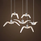 Five white bird-shaped pendants from this Clérachic fixture glow warm against a dark brown backdrop.