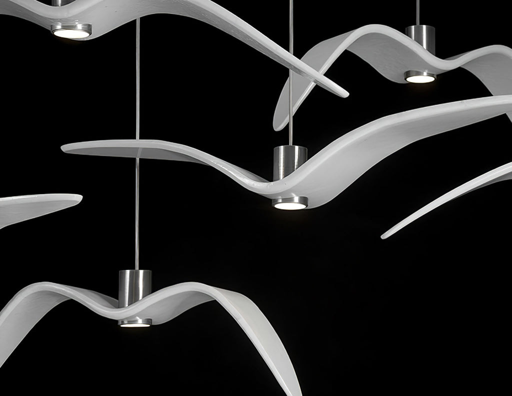 Overlapping white bird-shaped pendants from this Clérachic fixture cross wings closely, lit against a black backdrop.