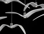 Overlapping white bird-shaped pendants from this Clérachic fixture cross wings closely, lit against a black backdrop.
