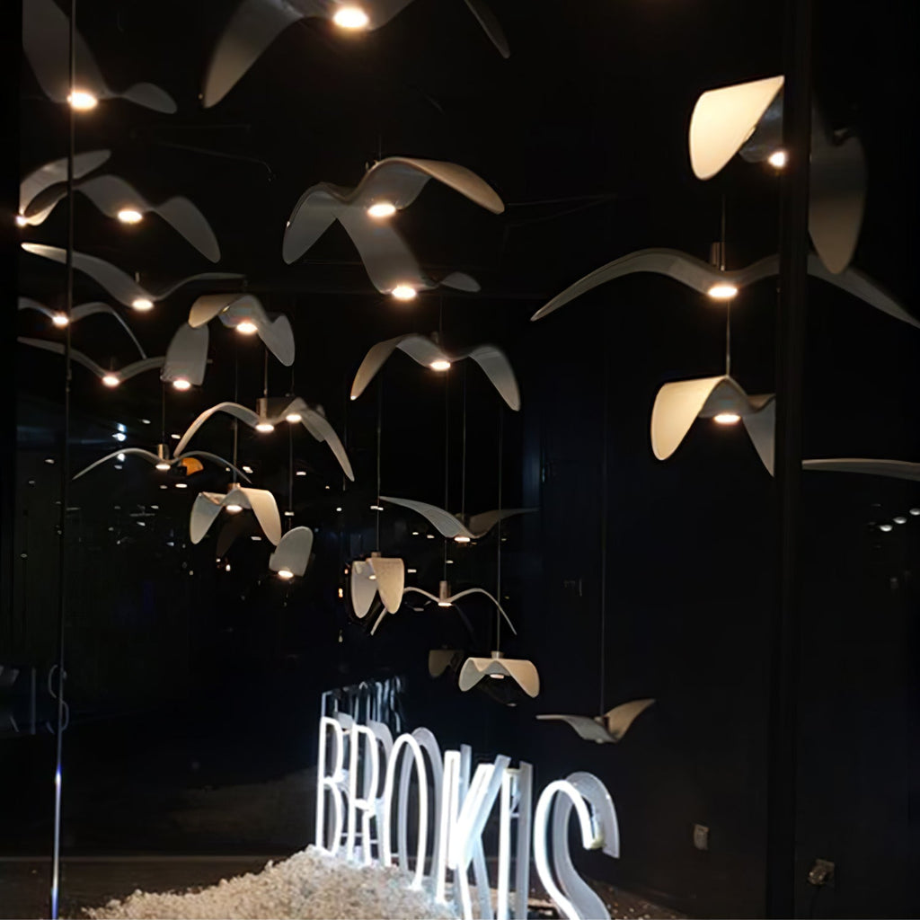 Illuminated white bird pendants from this Clérachic light glow warm at night above a reflective shopfront display.
