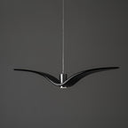 A black bird-shaped pendant from this Clérachic light hangs front-on with its wings at their widest, on a plain dark-grey backdrop.