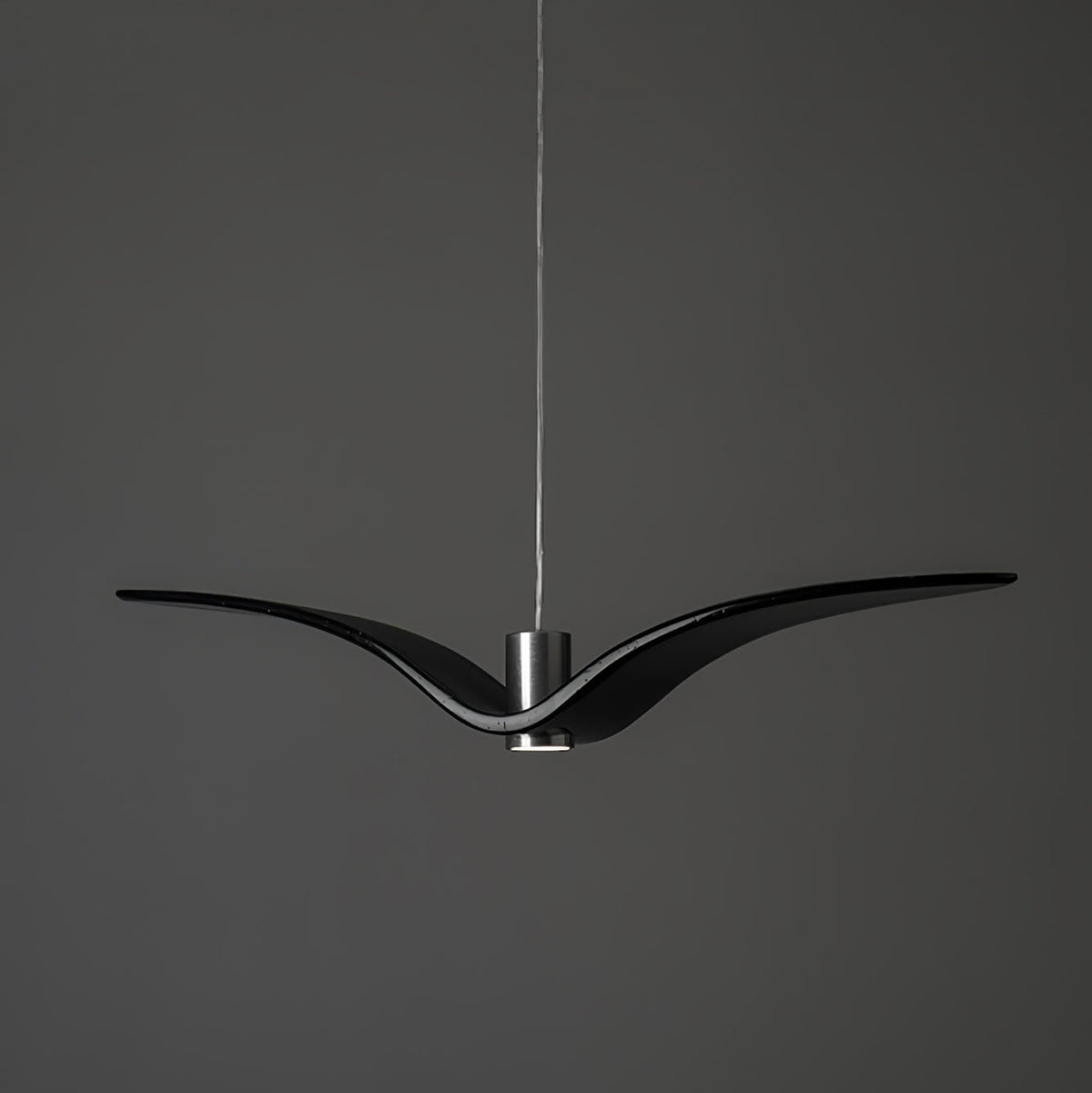 A black bird-shaped pendant from this Clérachic light hangs front-on with its wings at their widest, on a plain dark-grey backdrop.