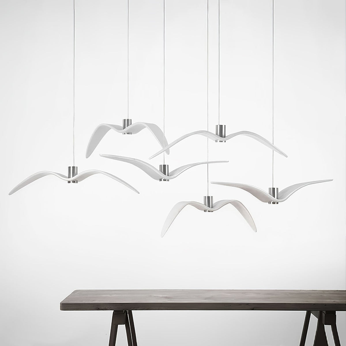 White bird-shaped pendants from this Clérachic light hang above a dark wood table on a plain white backdrop.