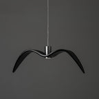 A black bird-shaped pendant from this Clérachic light hangs front-on with wide-spread wings, on a plain dark-grey backdrop.