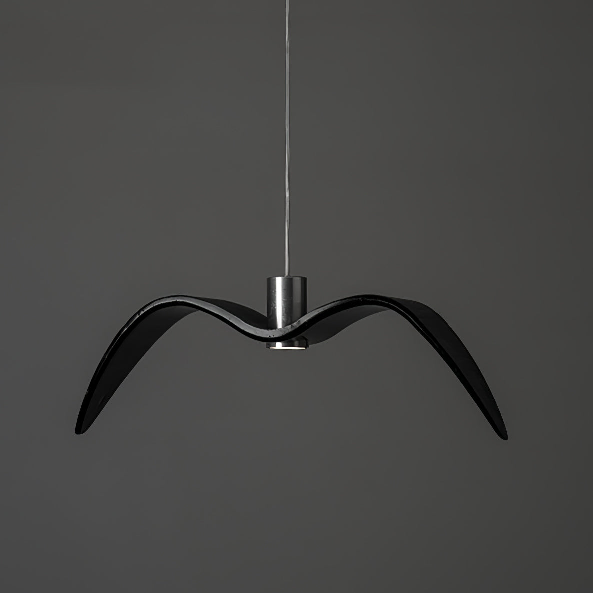 A black bird-shaped pendant from this Clérachic light hangs front-on with wide-spread wings, on a plain dark-grey backdrop.