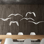 A flock of white bird-shaped pendants from Clérachic hangs above a wooden dining table against a dark panelled wall.