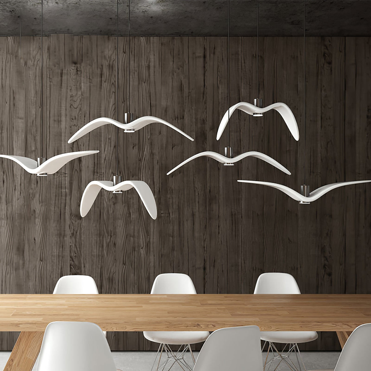 A flock of white bird-shaped pendants from Clérachic hangs above a wooden dining table against a dark panelled wall.