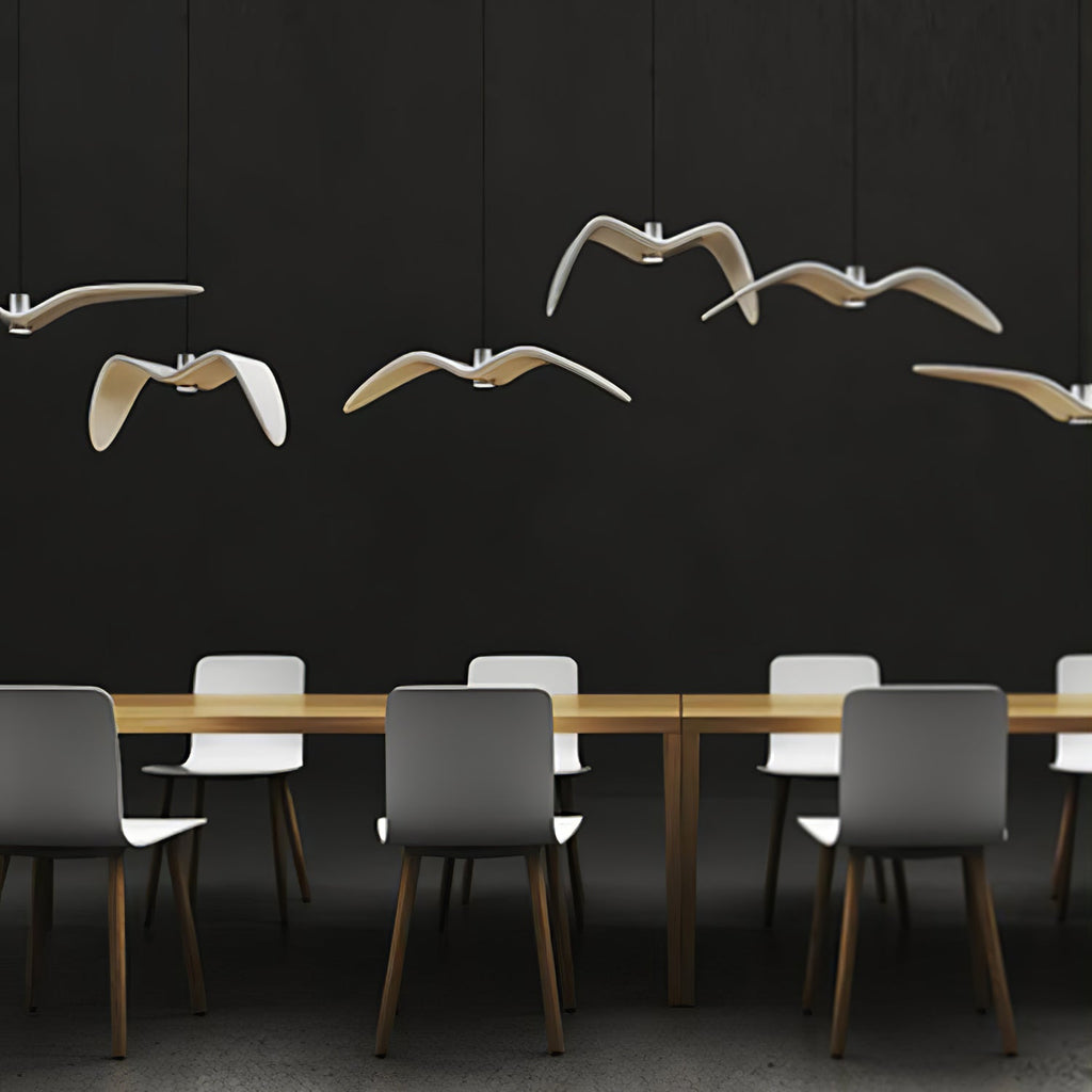 Bird-shaped pendants from this Clérachic fixture glow warm above a long table with grey chairs, against a dark wall.