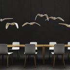 Bird-shaped pendants from this Clérachic fixture glow warm above a long table with grey chairs, against a dark wall.