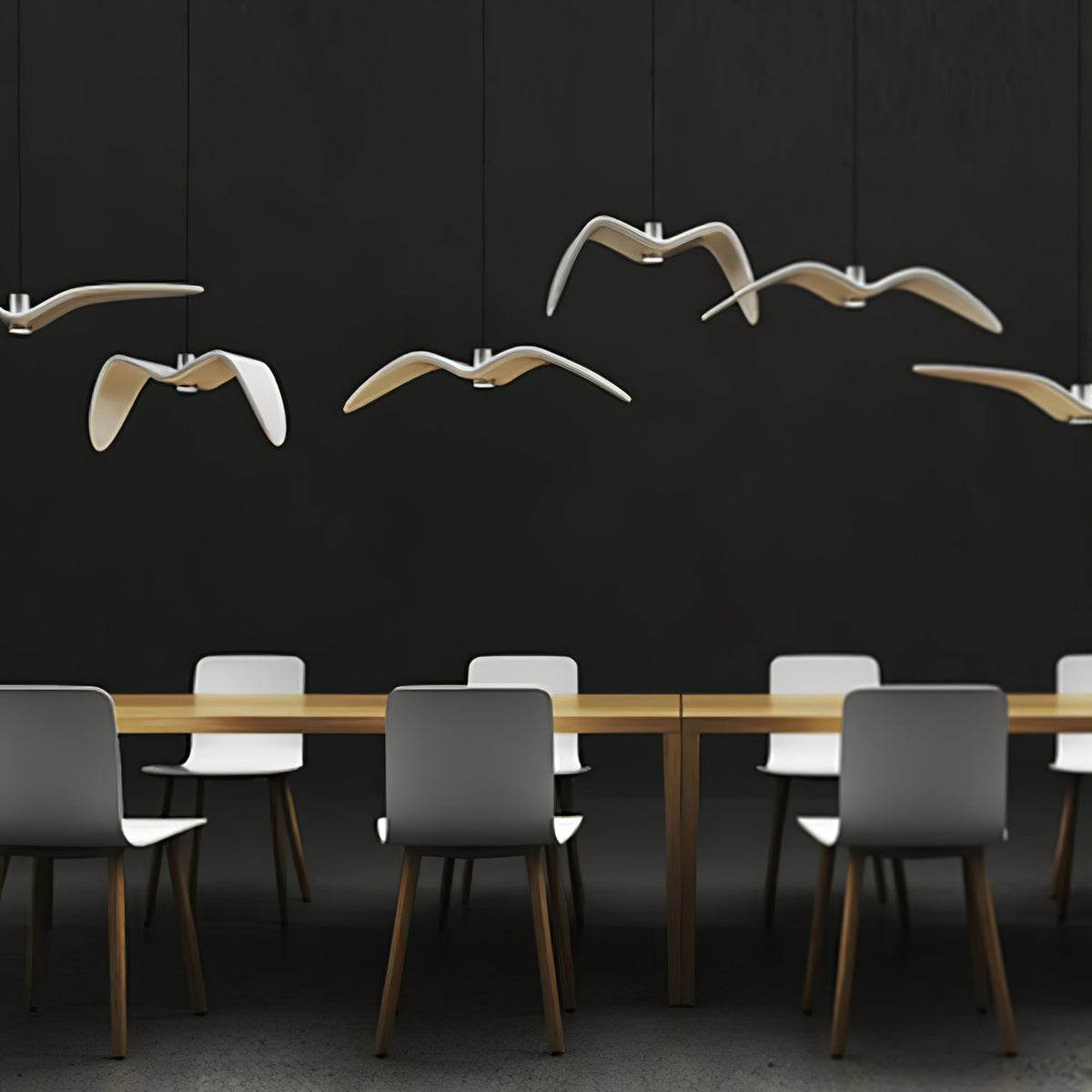 Bird-shaped pendants from this Clérachic fixture glow warm above a long table with grey chairs, against a dark wall.