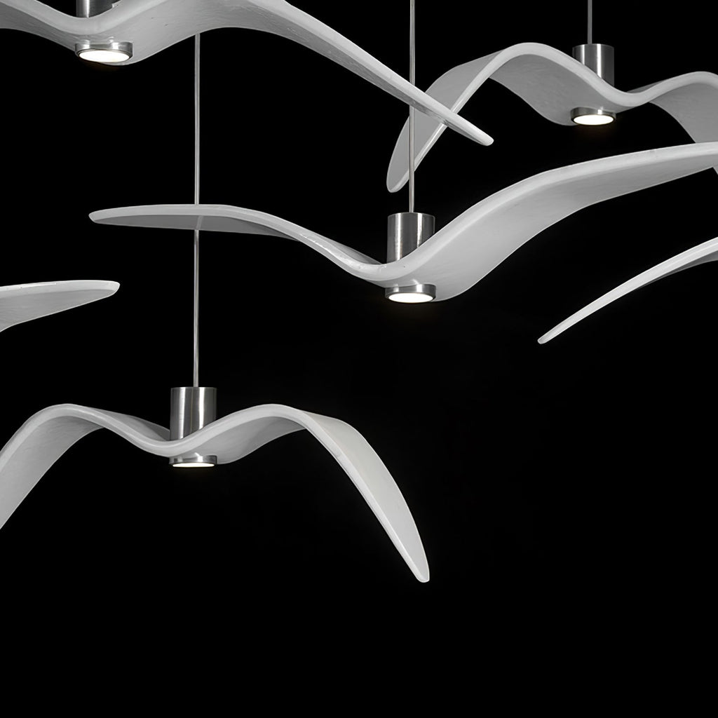 Close view of overlapping white bird-shaped pendants from this Clérachic fixture, lit against a black backdrop.