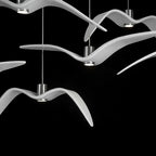Close view of overlapping white bird-shaped pendants from this Clérachic fixture, lit against a black backdrop.
