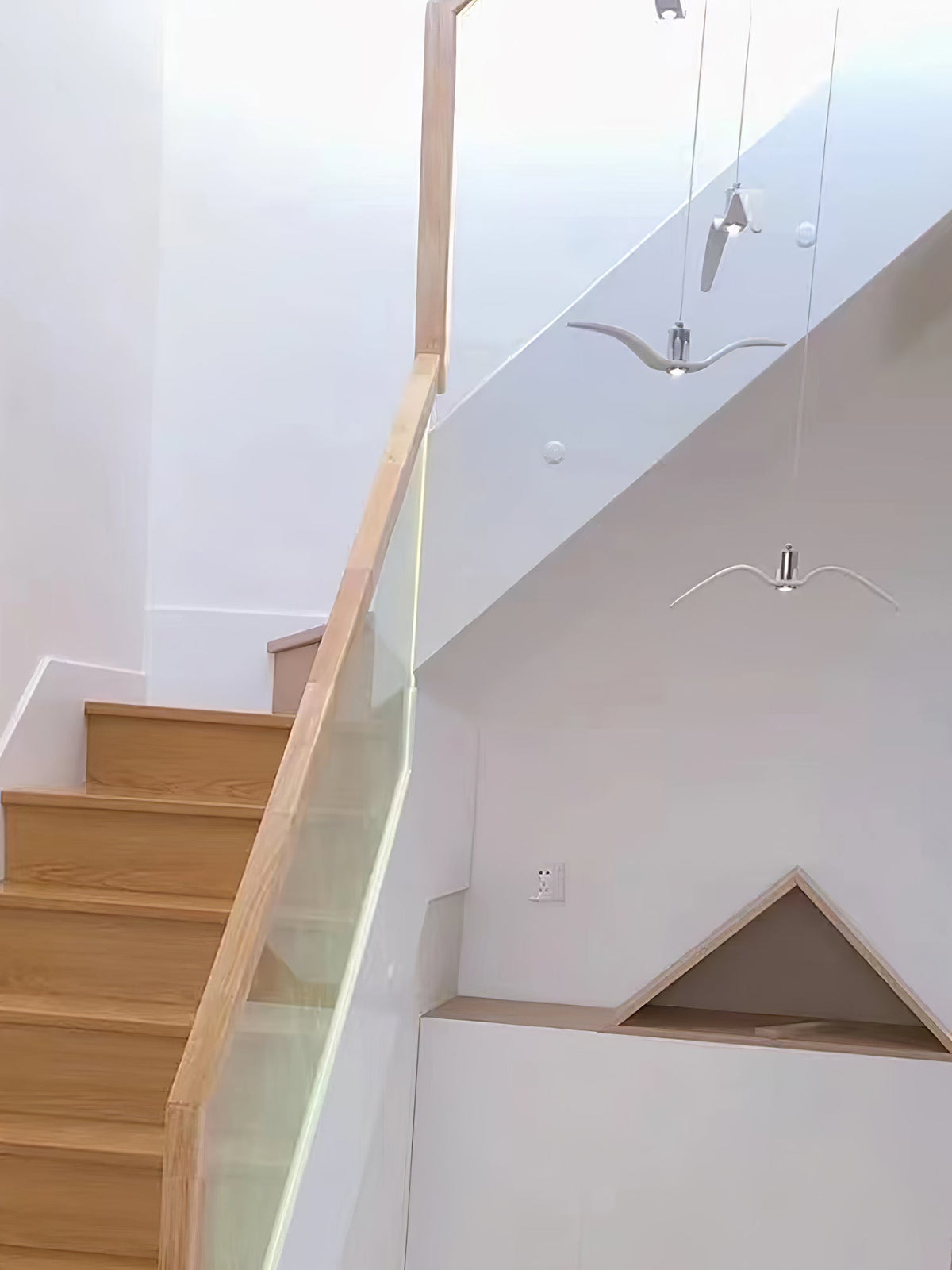 Small bird-shaped pendants from this Clérachic light hang near a wooden staircase with a glass railing.