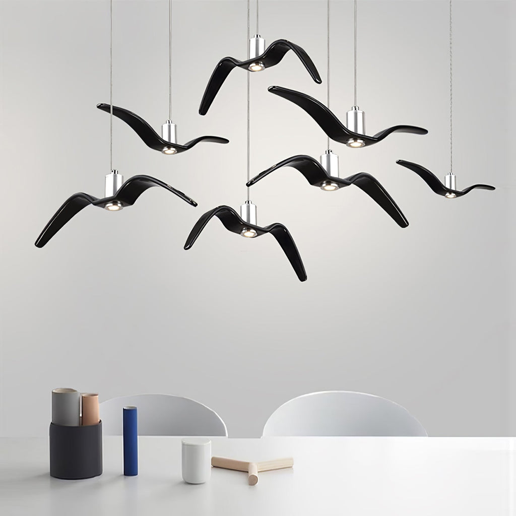 Black bird-shaped pendants from this Clérachic fixture hang above a table set with vases and decor, against a light-grey wall.