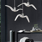Three white bird-shaped pendants from this Clérachic fixture hang at staggered lengths above a home office desk with a bin and plant.