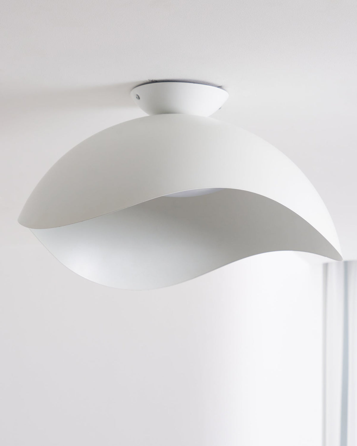 Seen from below near a window, the wave-cut underside of this Clérachic ceiling light lets soft light through.