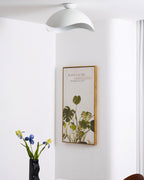Seen from a doorway, this Clérachic wave ceiling light hangs beside a framed plant print and a vase of flowers.