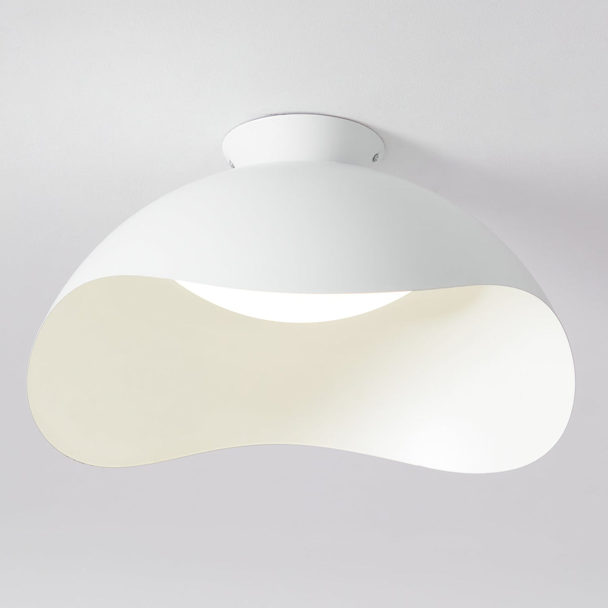 Close view of the wave-cut shade on this Clérachic ceiling light, with light spilling from the curved opening.