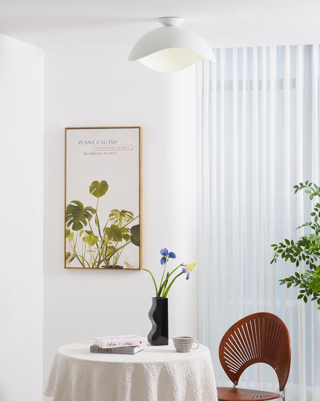 Above a round dining table set with books and a floral vase, this Clérachic ceiling light glows warm white.