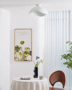A woven-back chair and a botanical print sit beneath this Clérachic ceiling light in a bright dining corner.