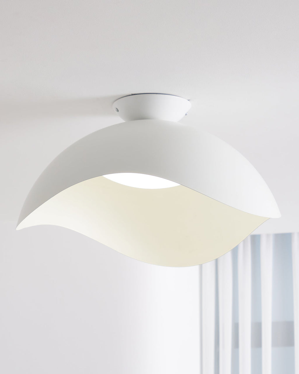 Near a window with sheer striped curtains, this Clérachic wave ceiling light glows warm from below.